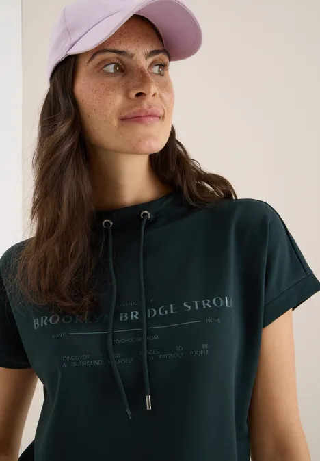 Frau mit dunklem Shirt und rosa Cap blickt zur Seite.